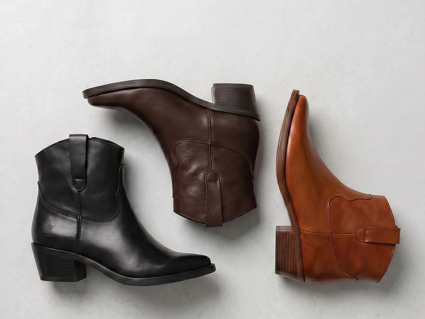 Drei Evie Western-Stiefeletten von Apple of Eden in Schwarz, Dunkelbraun und Cognac von oben fotografiert